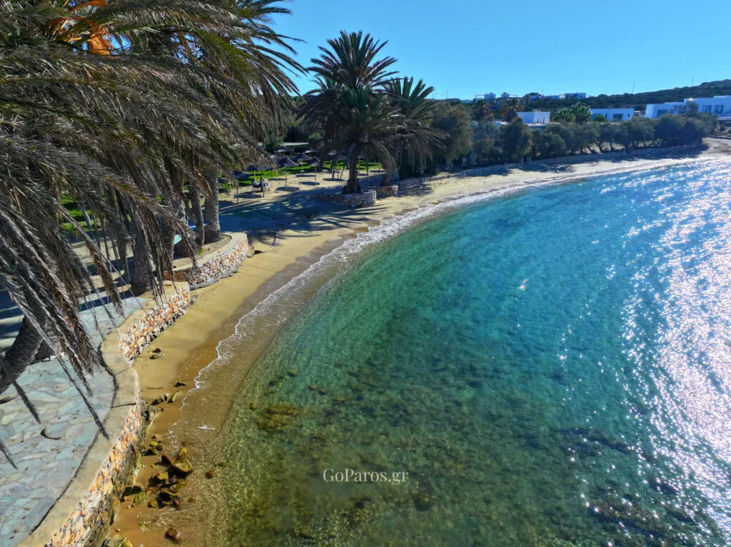 Agia Irini Beach, Paros, curved sandy shoreline with stone seawall walkway and clear water along the edge