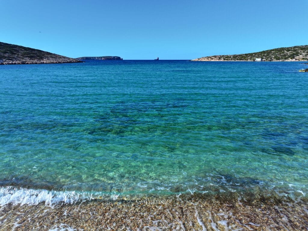 Agia Irini Beach, Paros, shoreline view of clear shallow water over pebbles with rocky islets on the horizon