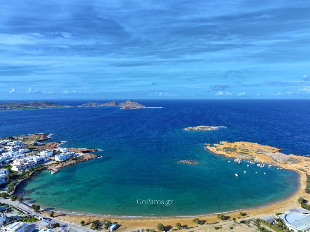 Agioi Anargyroi Beach, Paros, panoramic aerial view of the bay opening to the Aegean with offshore islets and boats moored near the beach
