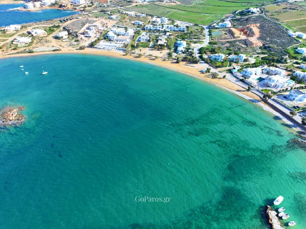Agioi Anargyroi Beach, Paros, drone view of the bay with the sandy beach, nearby villas, and green fields inland