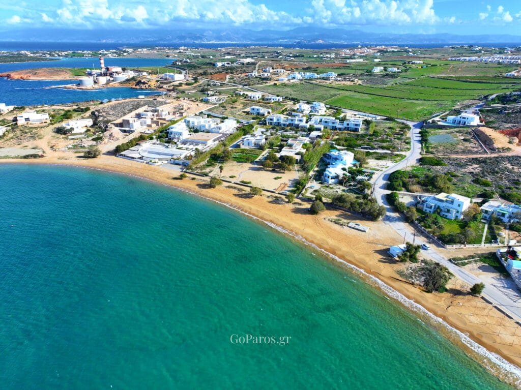 Agioi Anargyroi Beach, Paros, aerial view of the beach and coastal road with white villas, shallow turquoise water, and farmland in the background