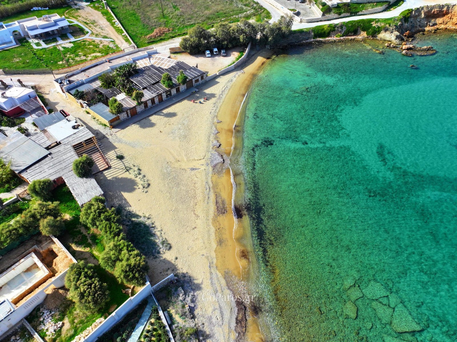 Delfini Beach, Paros, top-down aerial of the sandy beach and beachfront buildings beside clear water