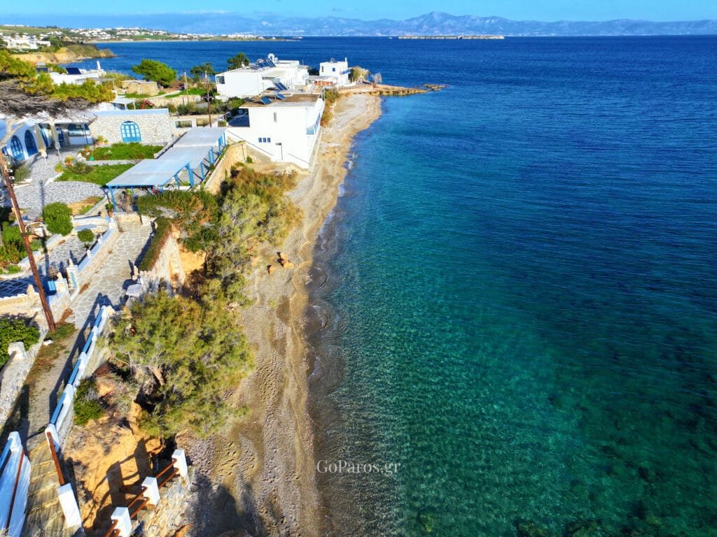 Sandy beach curve with a few people walking and calm blue water at Drios Beach, Paros.