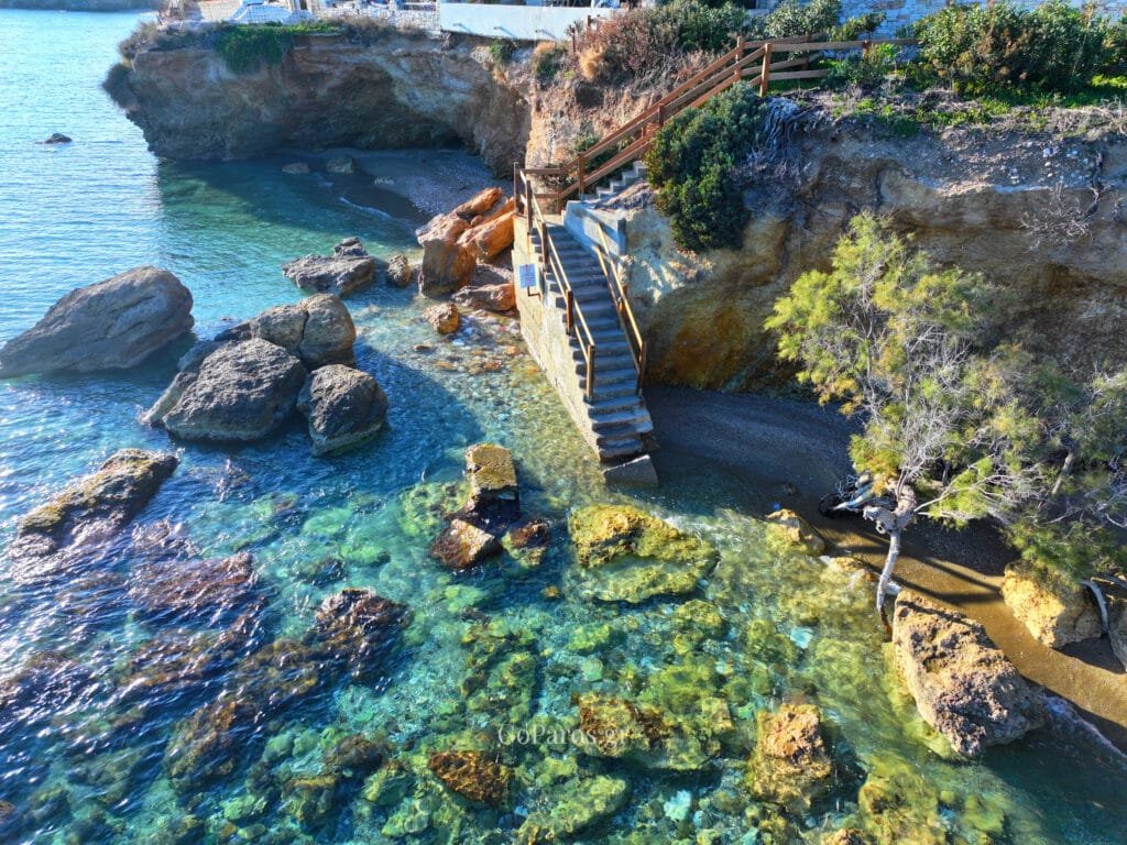 Wooden staircase down to a rocky cove with clear turquoise water at Drios Beach, Paros.