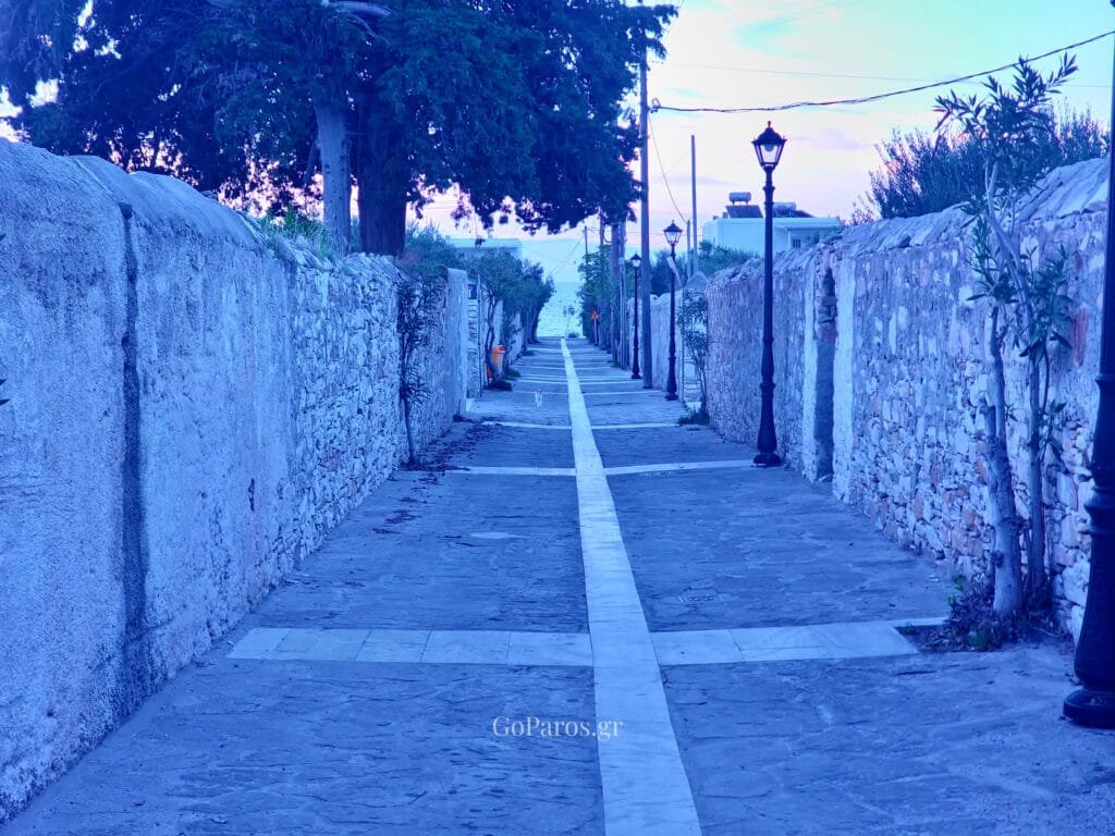 Drios, Paros, stone pedestrian lane between high walls with street lamps leading down to the sea