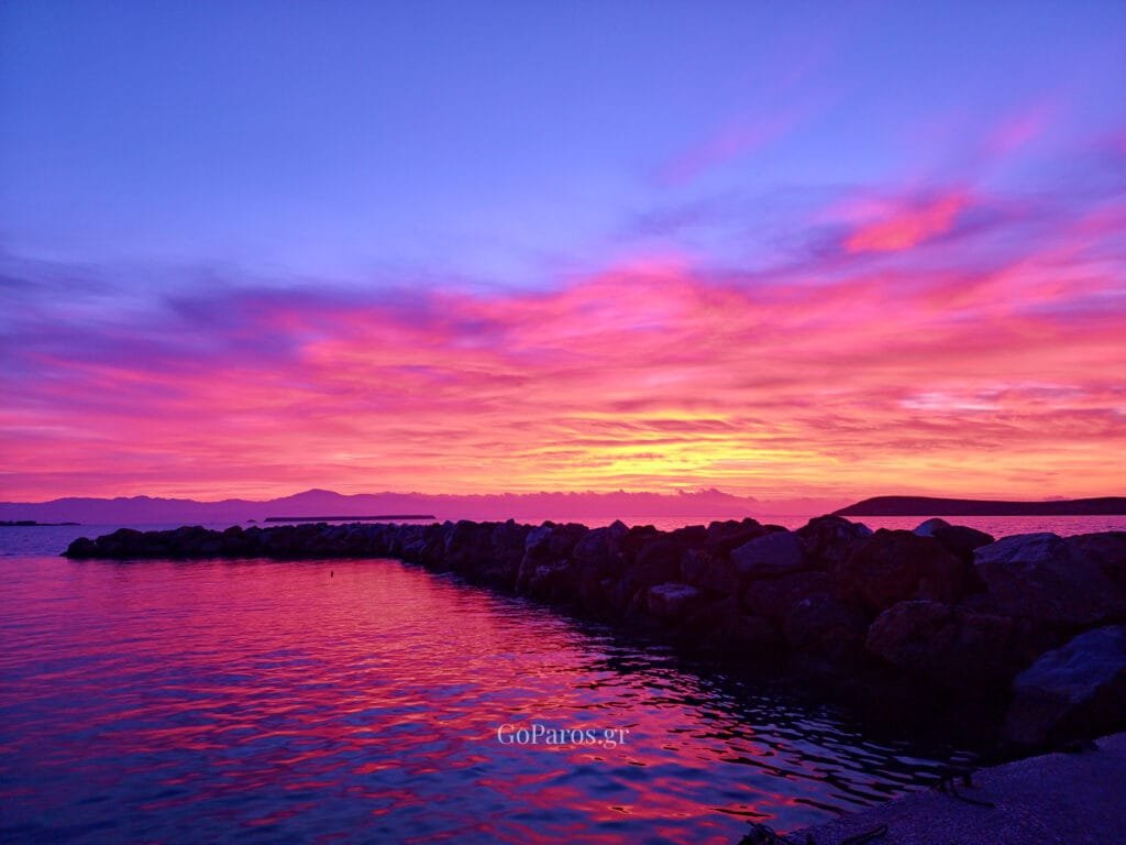 Drios, Paros, vivid pink sunrise over the sea with a rock breakwater and reflections on the water