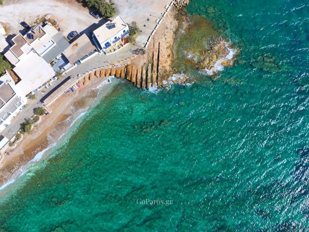 Drios, Paros, white waterfront building with a wooden staircase and balcony above a stone-paved quay