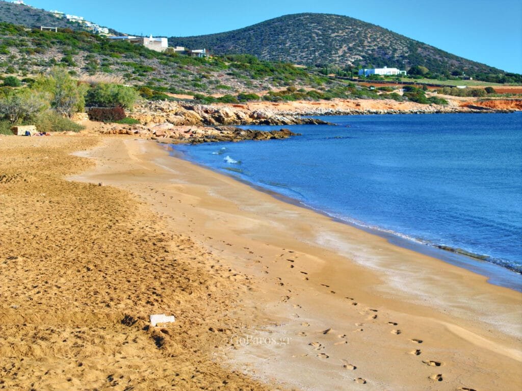 Long sandy shoreline at Faraggas Beach, Paros, with calm blue water and low hills in the background.