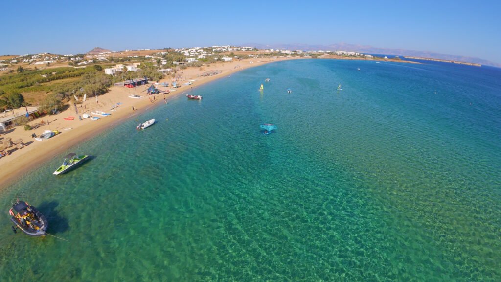 Aerial view of Golden Beach in Paros, long sandy bay with turquoise water, boats and windsurfers along the shoreline.
