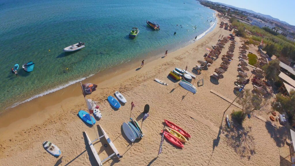 Aerial view of Golden Beach in Paros with kayaks, SUP boards and rows of sunbeds lined up on the sand beside the sea.