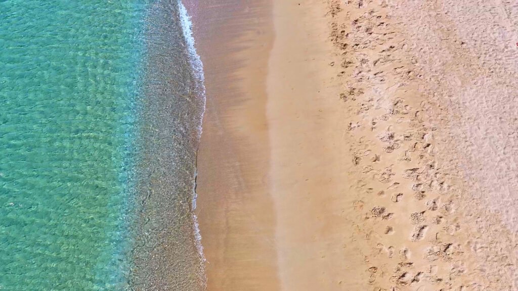 Close aerial view of Golden Beach in Paros, showing turquoise water meeting the sand with footprints along the beach.