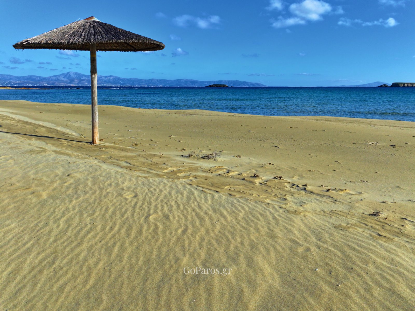 Straw beach umbrella on rippled sand at New Golden Beach, Paros