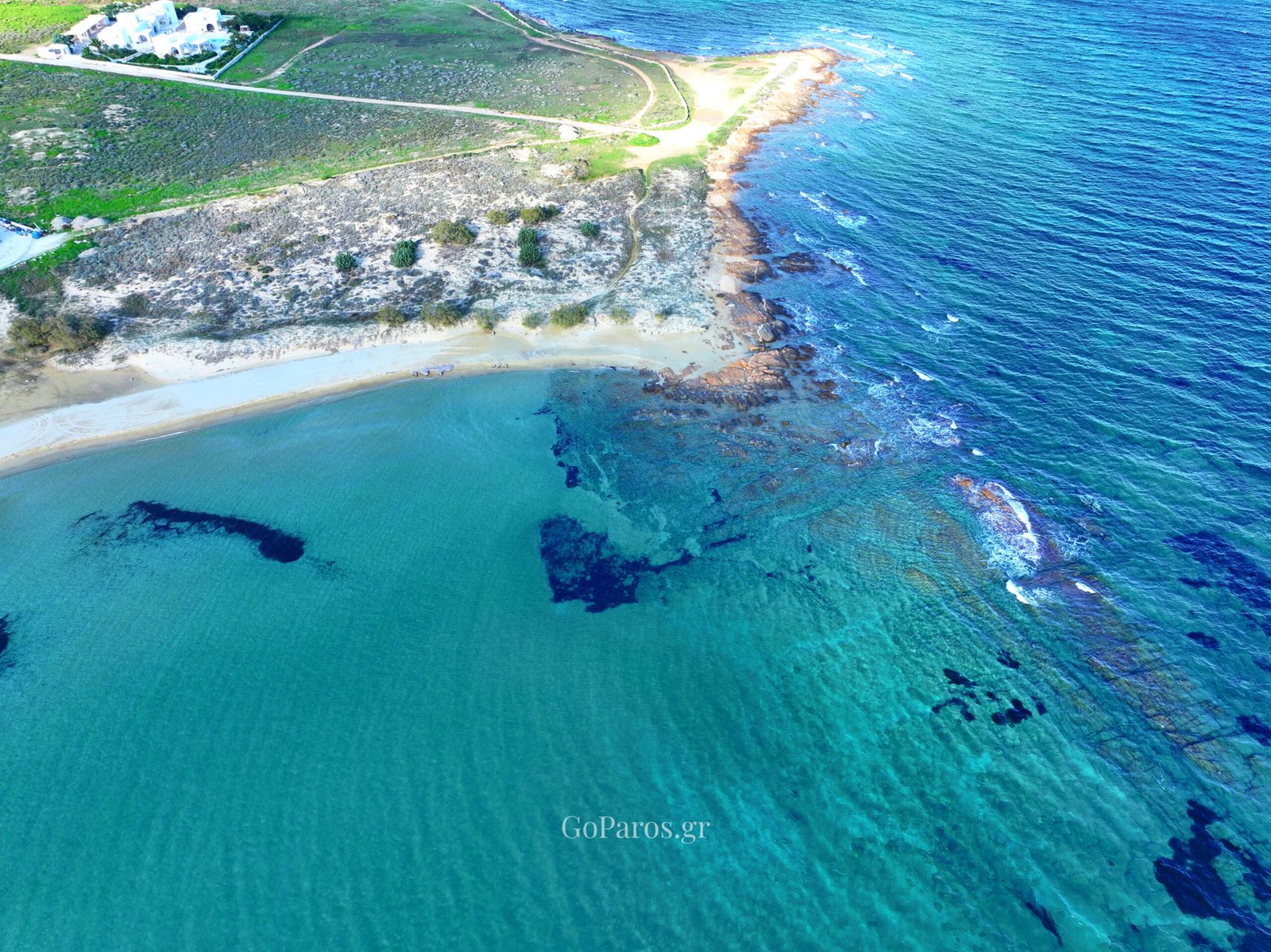 Drone view of New Golden Beach coastline and rocky reef in clear water, Paros