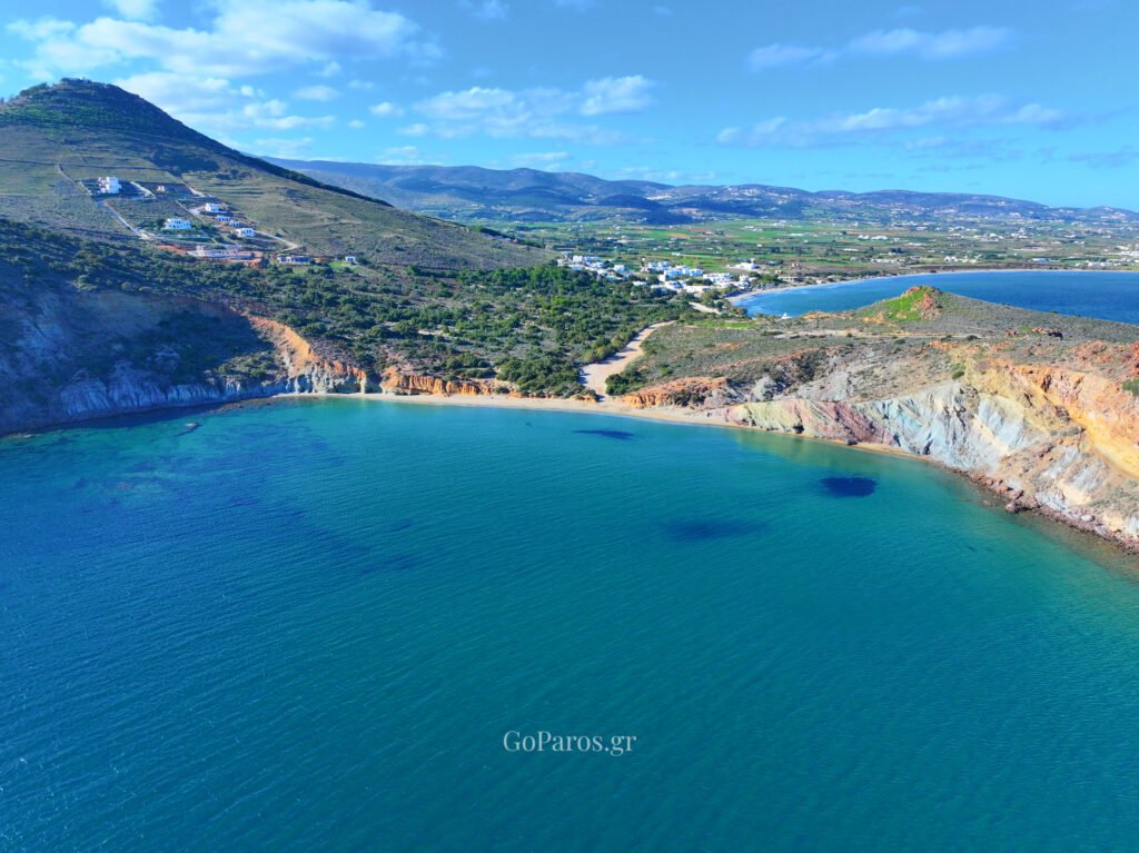 Aerial view of Kalogeros Beach bay in Paros with turquoise water and colorful cliffs.