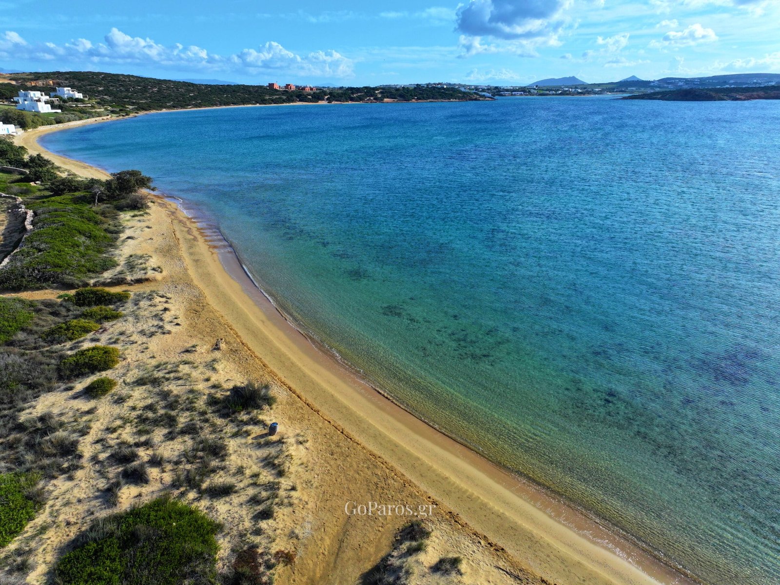 Laggeri Beach, Paros, aerial coastline view with a pier, clear water, and distant hills across the bay.