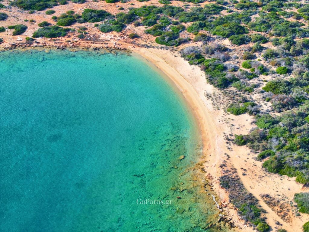 Laggeri Beach, Paros, shallow clear water beside a sandy cove with rocks and low coastal scrub.