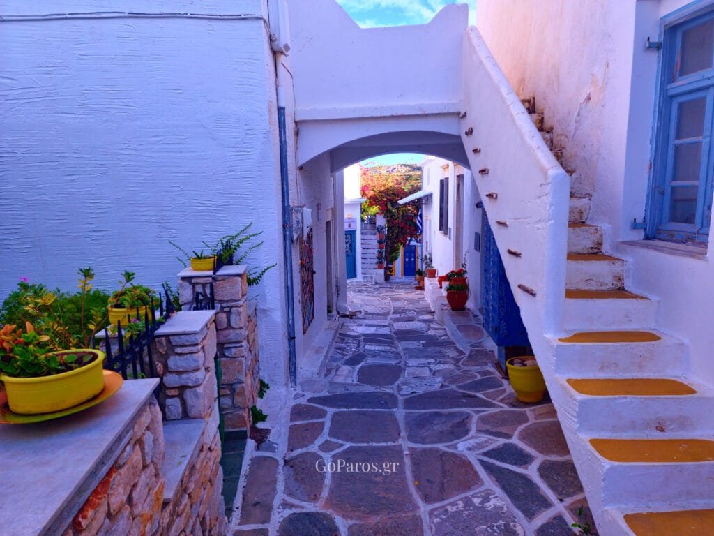 Lefkes, Paros, arched passageway with yellow-painted steps, blue door, and potted plants along the stone lane