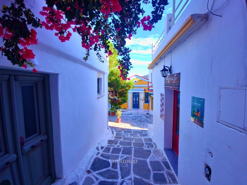 Lefkes, Paros, narrow whitewashed lane leading to a yellow building with blue door and bougainvillea overhead