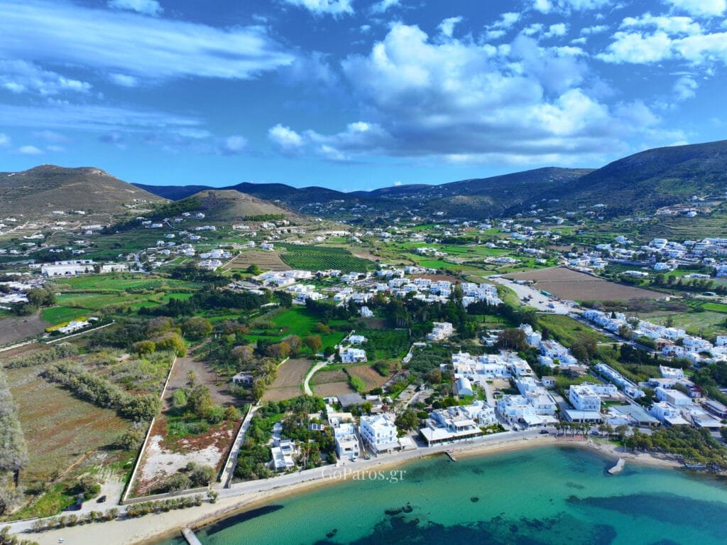 Livadia Beach, Paros, wide aerial view of the coastline with the beach in the foreground and Parikia valley, hills, and clouds inland