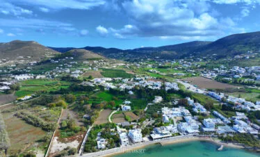 Livadia Beach, Paros, wide aerial view of the coastline with the beach in the foreground and Parikia valley, hills, and clouds inland