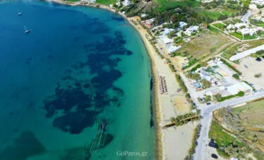 Livadia Beach, Paros, aerial view of the long sandy shoreline with beach umbrellas, a beach court, and clear water with dark seabed patches