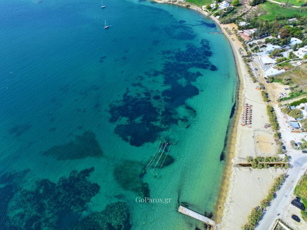 Livadia Beach, Paros, oblique aerial view of the beach and bay with a small pier, umbrellas on the sand, and boats offshore