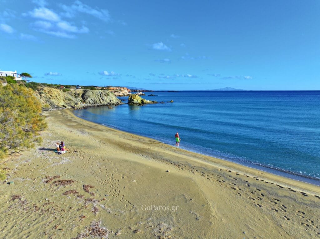 Lolantonis Beach on Paros with a sandy shoreline, rocky headland, and calm blue water.