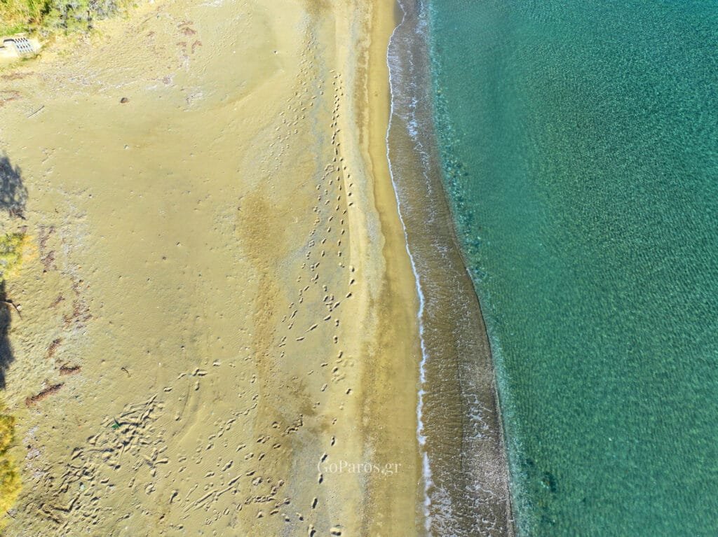 Top down drone shot of footprints on the sand and the clear waterline at Lolantonis Beach, Paros.