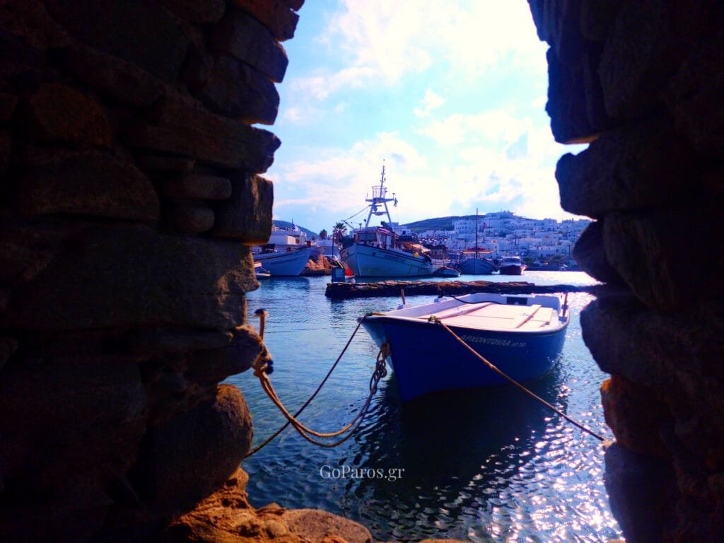 Naoussa, Paros, small blue boat moored in the harbor framed through a gap in a stone wall