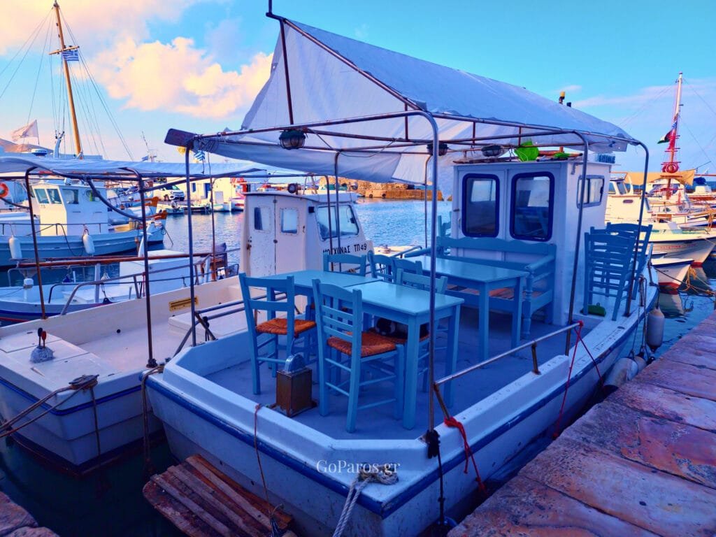 Naoussa, Paros, fishing boat moored in the harbor with blue tables and chairs on deck