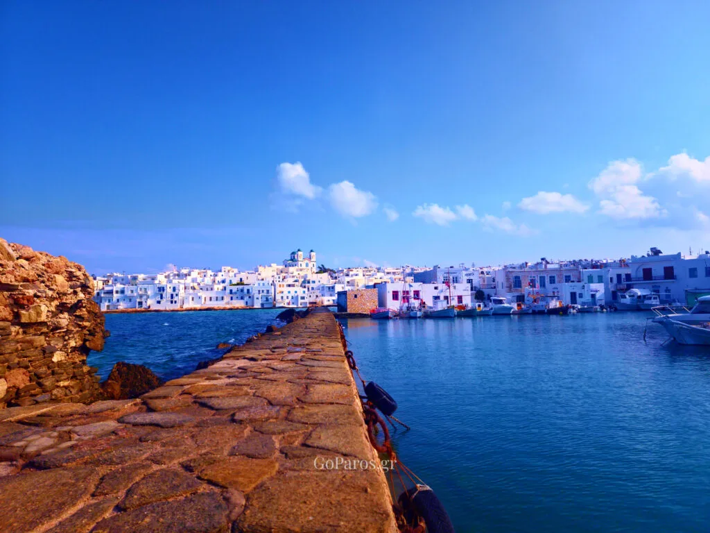 Naoussa, Paros, stone pier leading toward the harbor with white buildings and boats in the distance