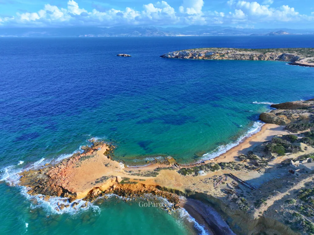 Palio Karnagio Beach, Paros, wide aerial of bay with turquoise shallows, deep blue sea, and distant mountains under clouds
