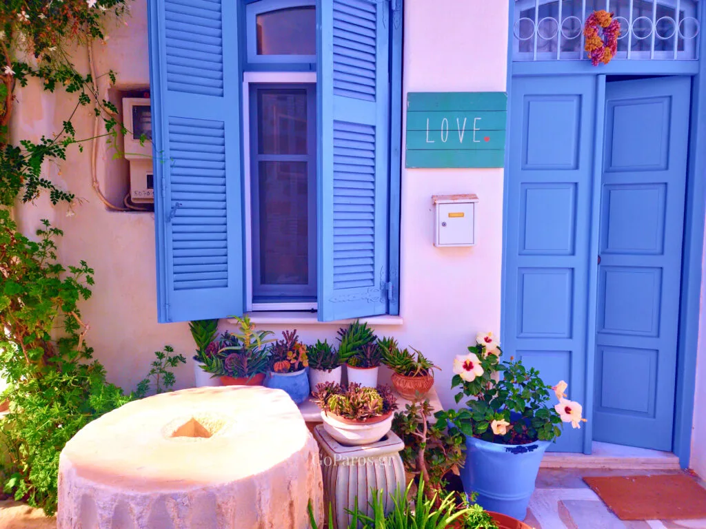 Parikia, Paros, blue shutters and door on a white house with potted plants and a “LOVE” sign