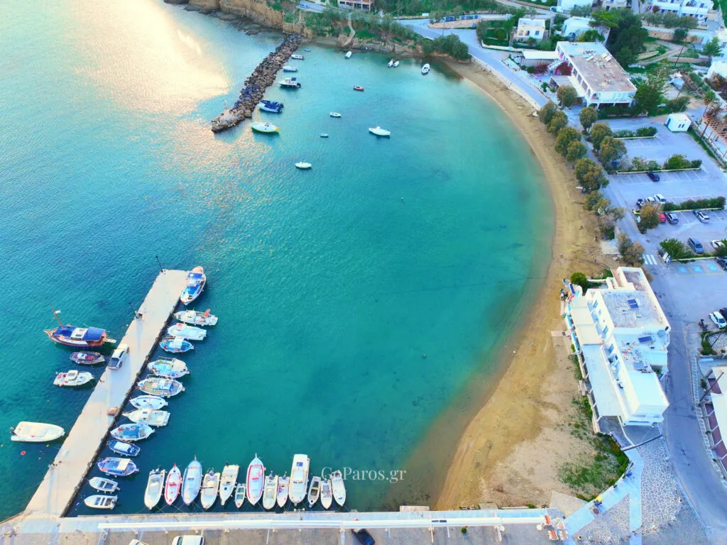Aerial view of Piso Livadi Beach, Paros, curved sandy bay with pier and clear turquoise sea.