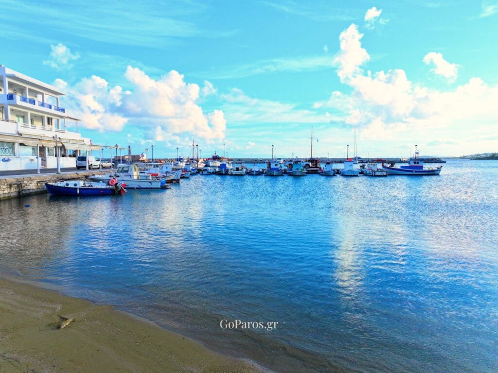 Piso Livadi Beach, Paros, harbor scene with fishing boats and waterfront buildings.