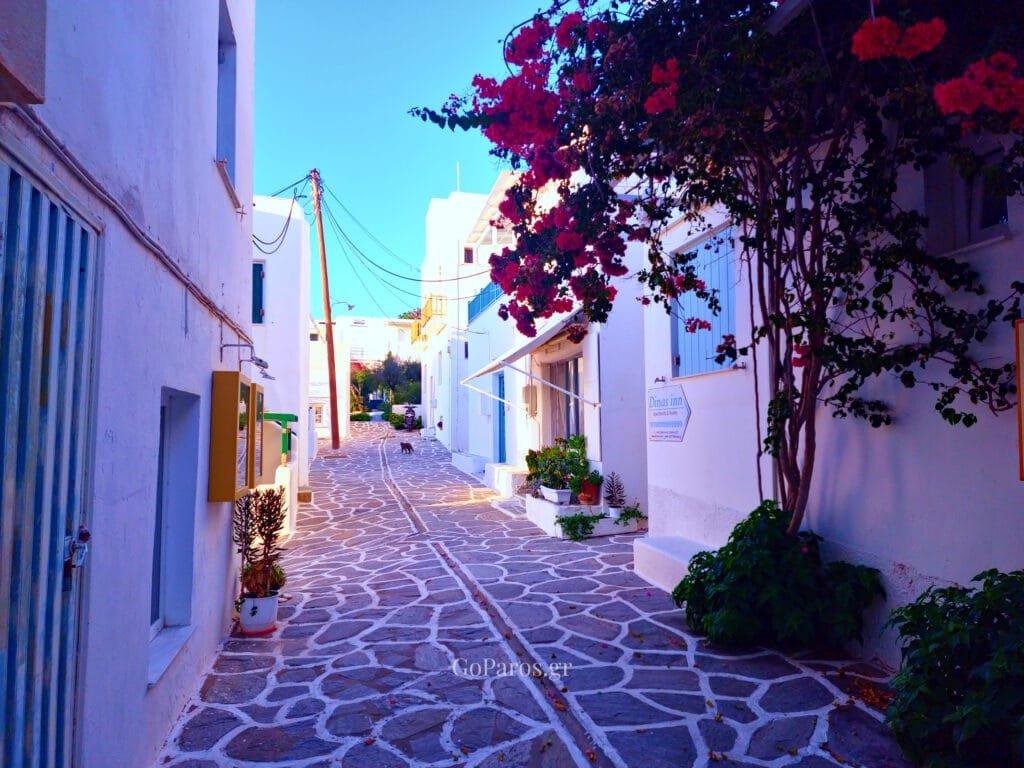 Piso Livadi, Paros, cobbled lane with a bright pink door and hibiscus flowers framing the walkway.