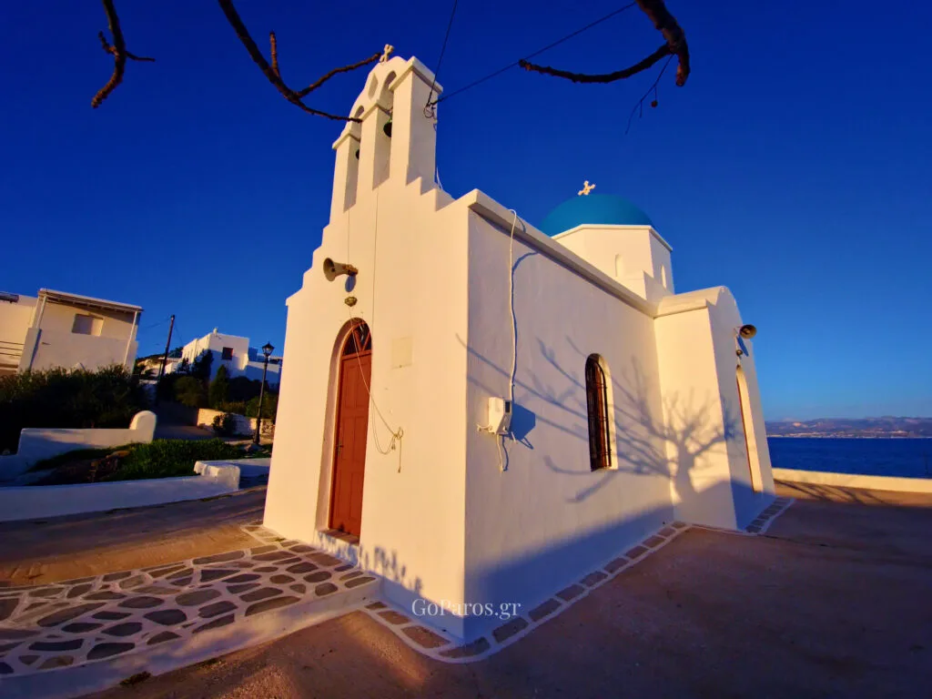 Piso Livadi, Paros, white seafront chapel with a blue dome and arched doorway in late afternoon light.
