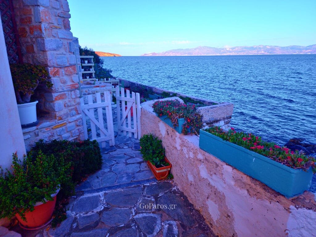 Piso Livadi, Paros, seafront stone walkway beside the water with planters and a small gate overlooking the Aegean.