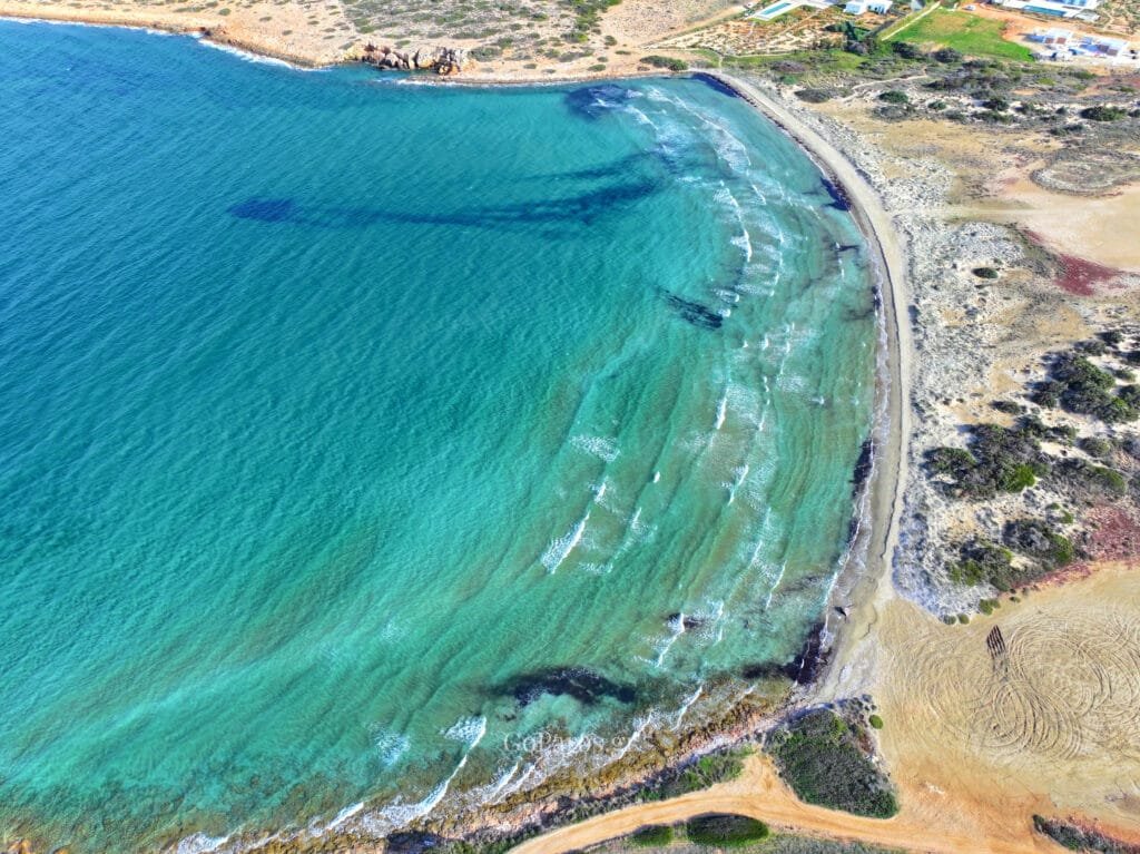 Platia Ammos Beach, Paros, top-down aerial of sandy shoreline beside a rocky outcrop with clear turquoise water