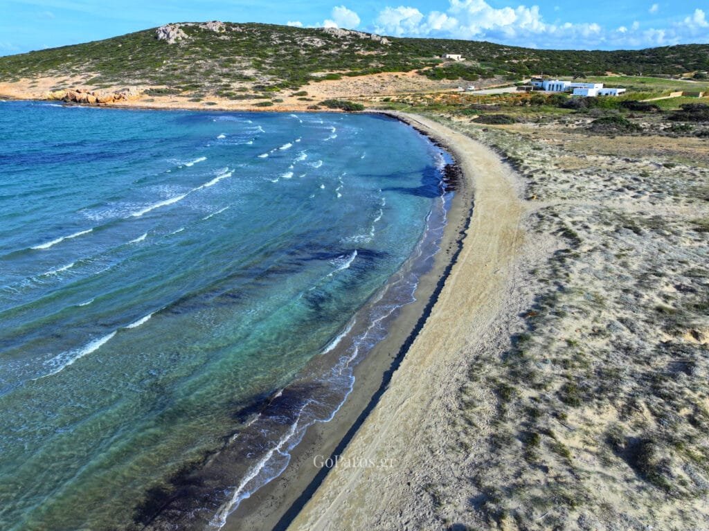 Platia Ammos Beach, Paros, wide aerial of a bay with turquoise shallows, deep blue sea, and distant mountains under clouds