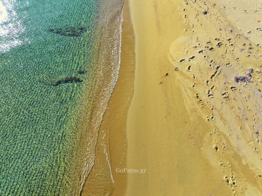 Top-down view of clear water and sandy shoreline with footprints at Punda Beach East, Paros.