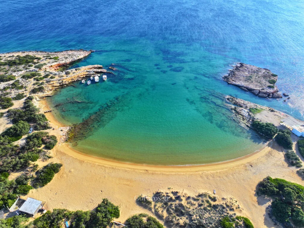 Small Santa Maria Beach, Paros, aerial view of a sheltered lagoon with sandy beach, boats, and a rocky islet.