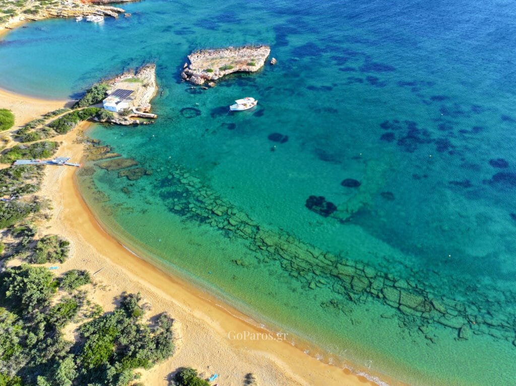 Small Santa Maria Beach, Paros, aerial view of sandy shoreline and turquoise water with beachfront buildings and trees.