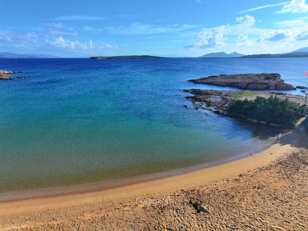 Small Santa Maria Beach, Paros, wide view of sandy beach and calm sea with white houses in the distance.