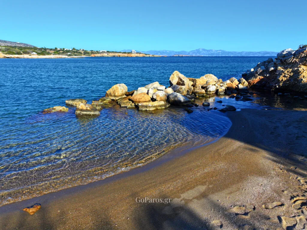 Small rocky cove at Tripiti Beach, Paros, with clear shallow water and stones along the shoreline.
