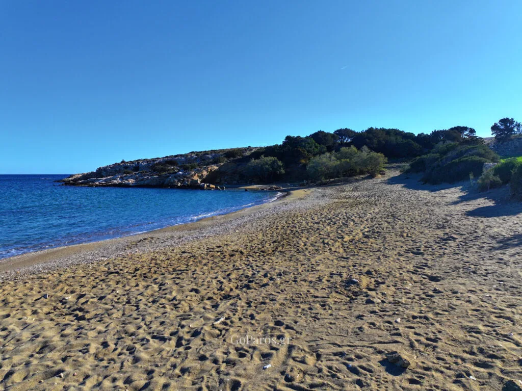 Wide view of Tripiti Beach in Paros with an open sandy stretch, calm sea, and a rocky headland.