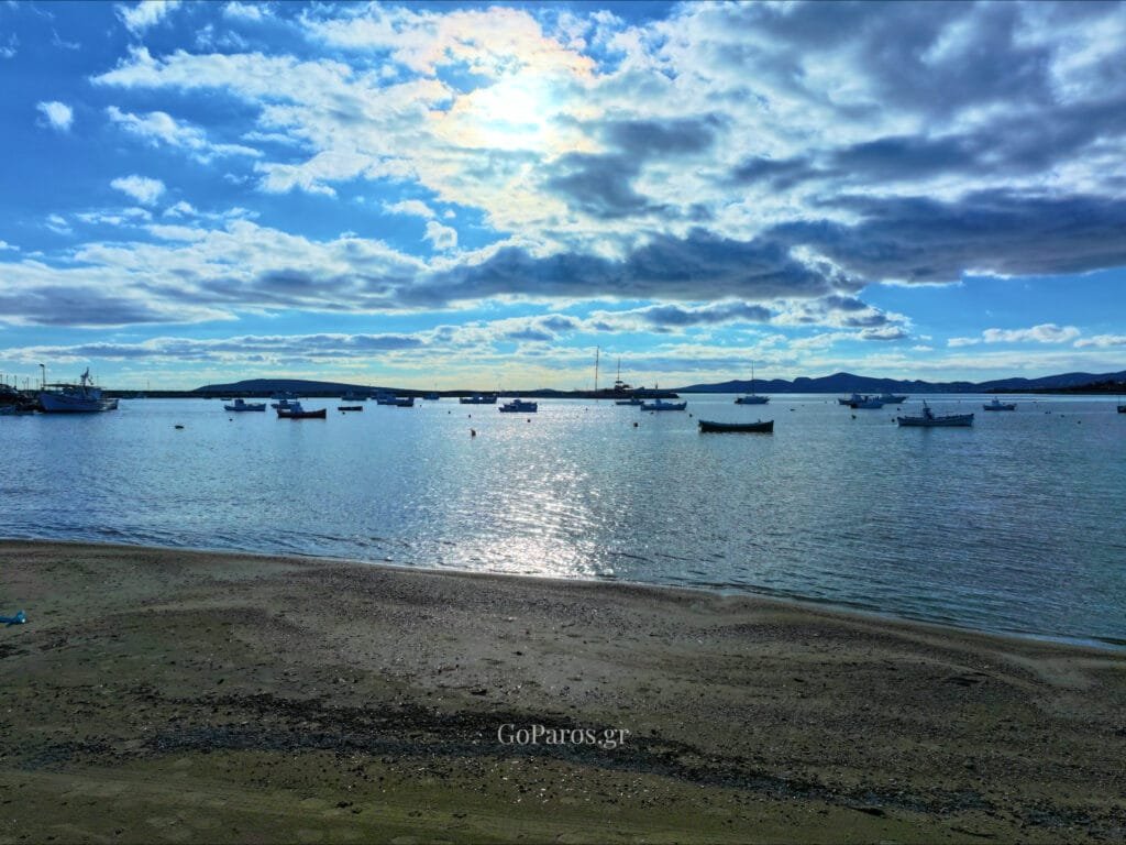 Aliki Beach, Paros, fishing boats on calm water with dramatic clouds and sun reflection