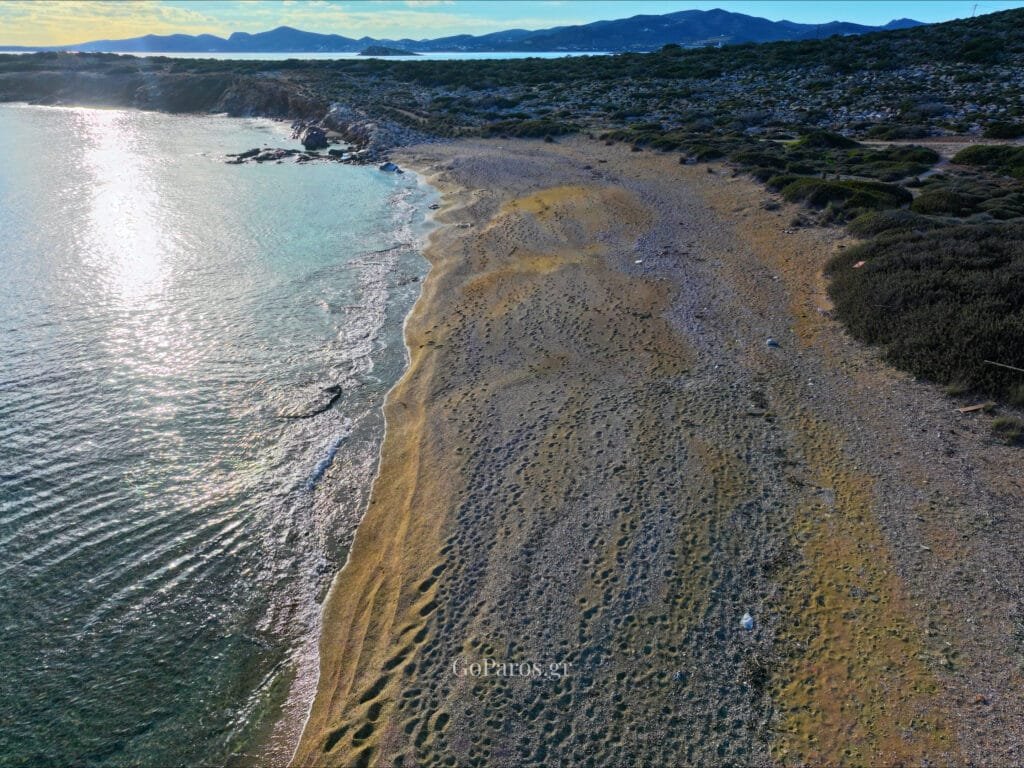 Makria Miti Beach, Paros, aerial view of a quiet pebble shoreline with sunlight reflecting on the water