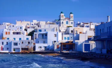 Naoussa, Paros seafront town view with white houses, a church, and waves along the shore