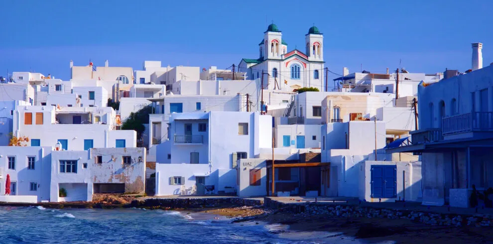 Naoussa, Paros seafront town view with white houses, a church, and waves along the shore